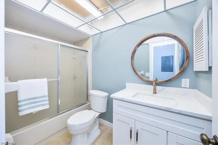 Bathroom with vanity, shower / bath combination with glass door, and light tile patterned floors