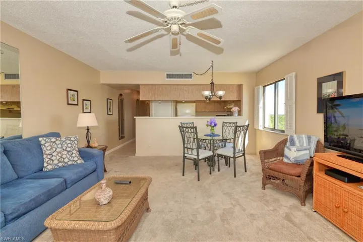 Living room featuring light carpet, a textured ceiling, and ceiling fan with notable chandelier