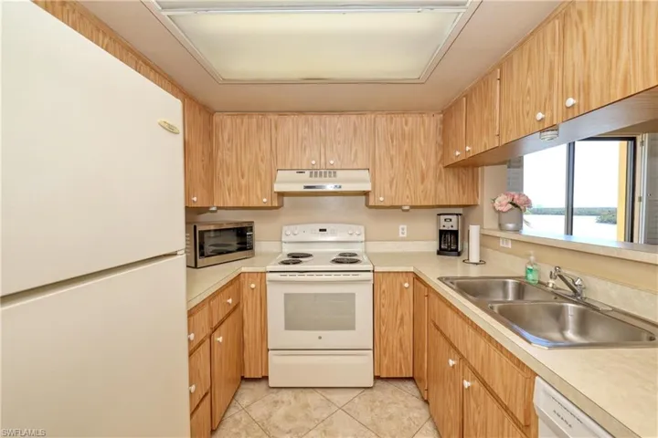 Kitchen featuring light tile patterned floors, white appliances, a water view, and sink