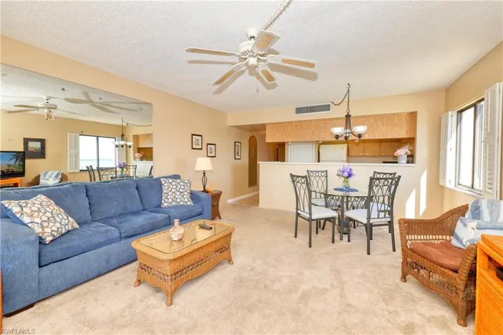 Living room featuring ceiling fan with notable chandelier, light colored carpet, and a textured ceiling
