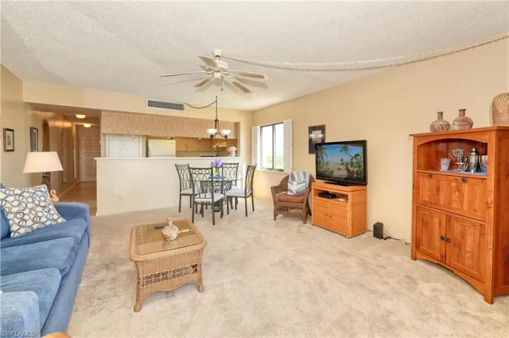 Carpeted living room with ceiling fan with notable chandelier and a textured ceiling