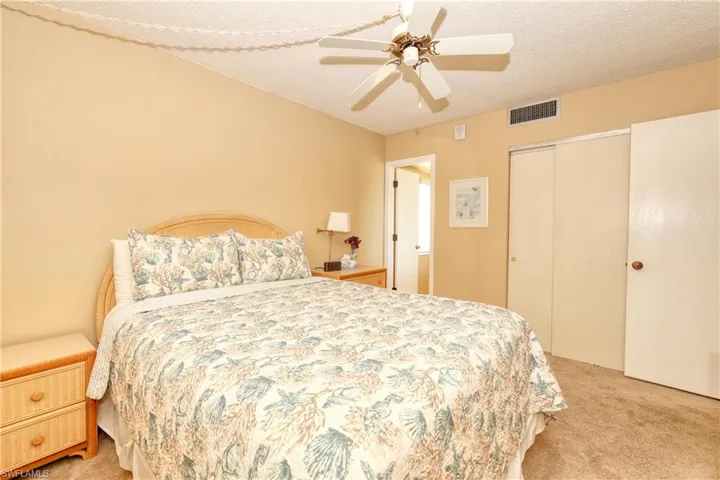 Bedroom featuring a textured ceiling, light carpet, visible vents, a ceiling fan, and a closet