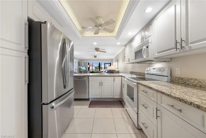 Kitchen with white cabinets, appliances with stainless steel finishes, a raised ceiling, light tile patterned floors, and crown molding