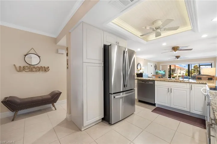 Kitchen with white cabinets, light tile patterned floors, a tray ceiling, ornamental molding, and stainless steel appliances