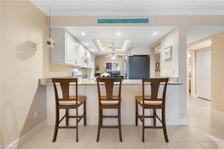 Kitchen with white appliances, a kitchen bar, light stone countertops, white cabinetry, and kitchen peninsula