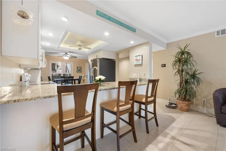 Kitchen featuring kitchen peninsula, white cabinetry, ornamental molding, a breakfast bar area, and stainless steel refrigerator
