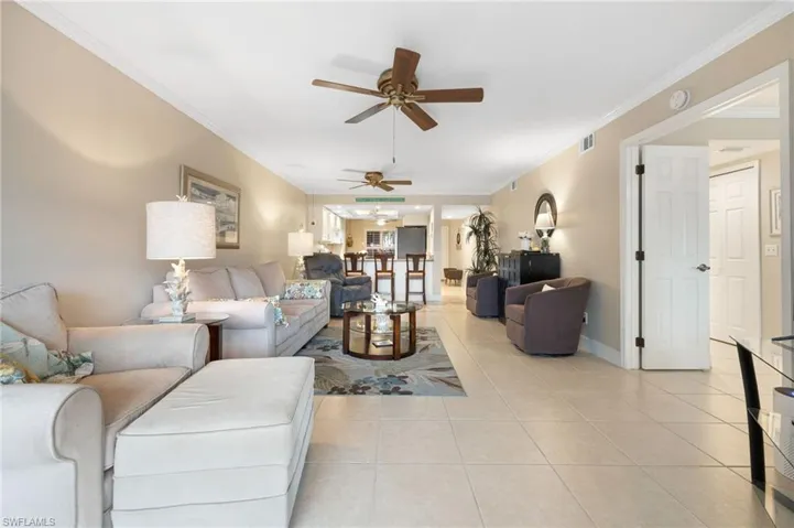 Living room with light tile patterned floors, ceiling fan, and ornamental molding