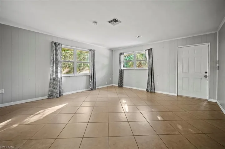 Living room featuring light tile patterned floors, plenty of natural light, ornamental molding, and wood walls