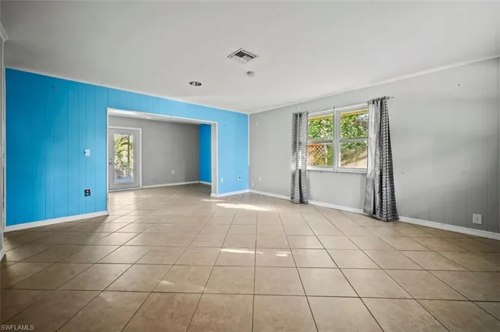 Living room featuring light tile patterned floors, ornamental molding, and wooden walls