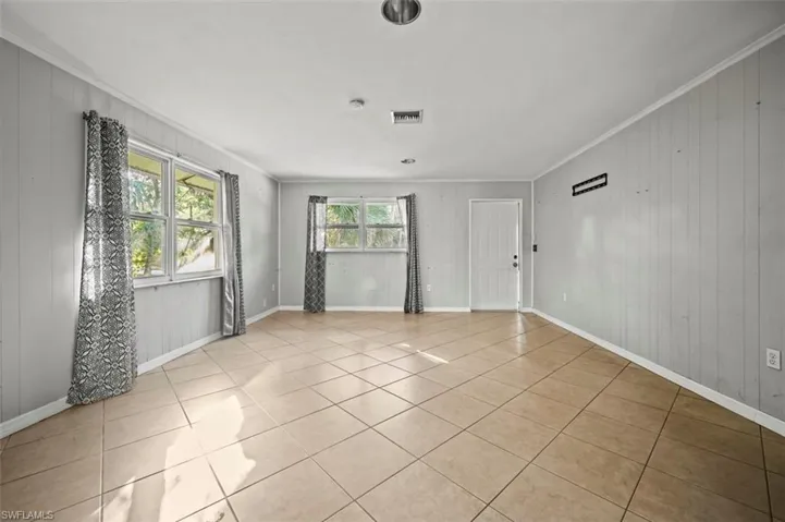 Living room featuring crown molding, light tile patterned floors, and wood walls