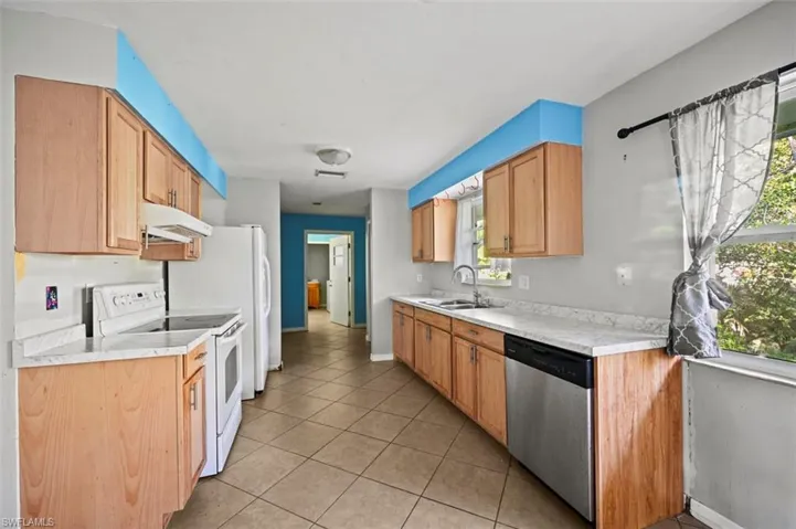 Kitchen with dishwasher, white electric range, light tile patterned flooring, and sink