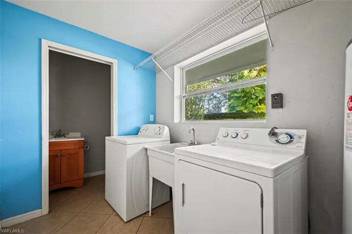 Laundry area with light tile patterned flooring, independent washer and dryer, and sink