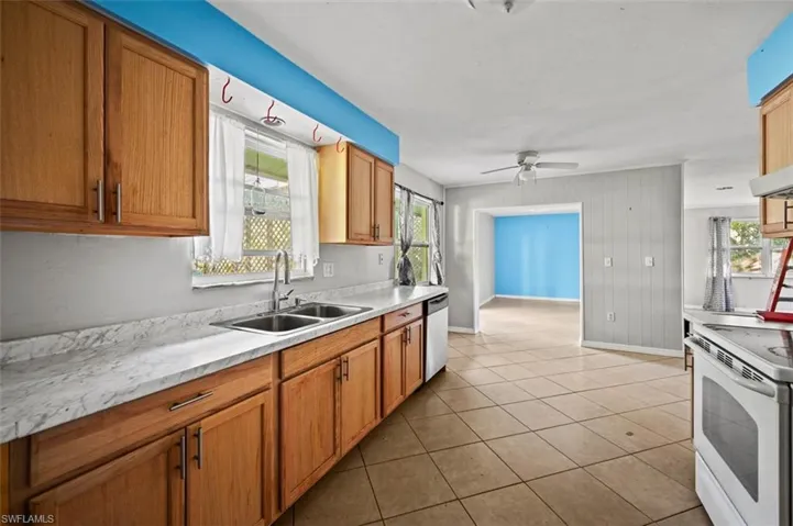 Kitchen with white electric stove, sink, stainless steel dishwasher, ceiling fan, and light tile patterned flooring