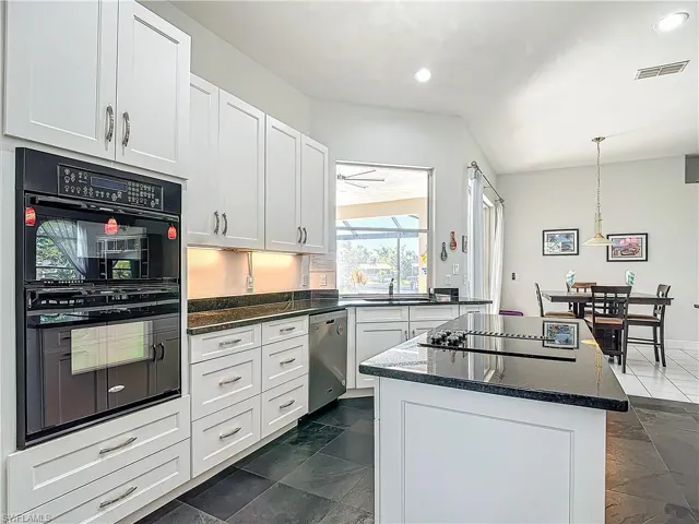 Kitchen with black appliances, white cabinetry, a kitchen island, decorative light fixtures, and dark stone counters