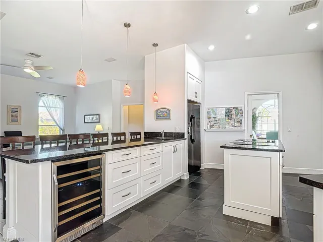 Kitchen with a kitchen breakfast bar, a kitchen island, white cabinetry, wine cooler, and hanging light fixtures