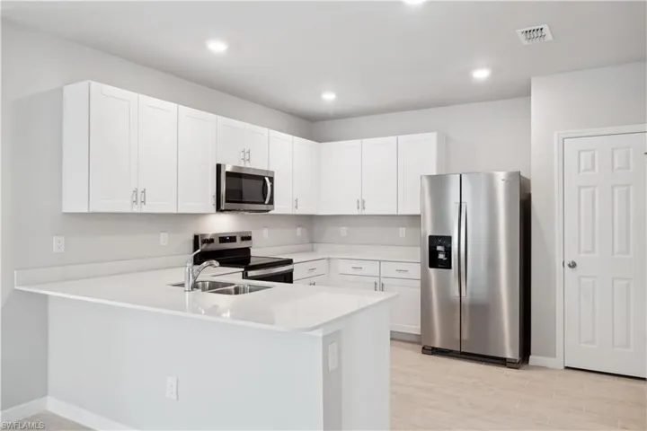 Kitchen with white cabinetry, sink, appliances with stainless steel finishes, light hardwood / wood-style flooring, and kitchen peninsula