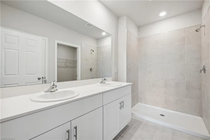 Bathroom featuring a tile shower and dual bowl vanity