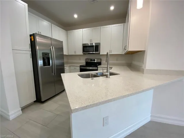 Modern kitchen featuring white shaker cabinetry, stainless steel appliances, speckled quartz countertops, and a double basin sink with a gooseneck faucet