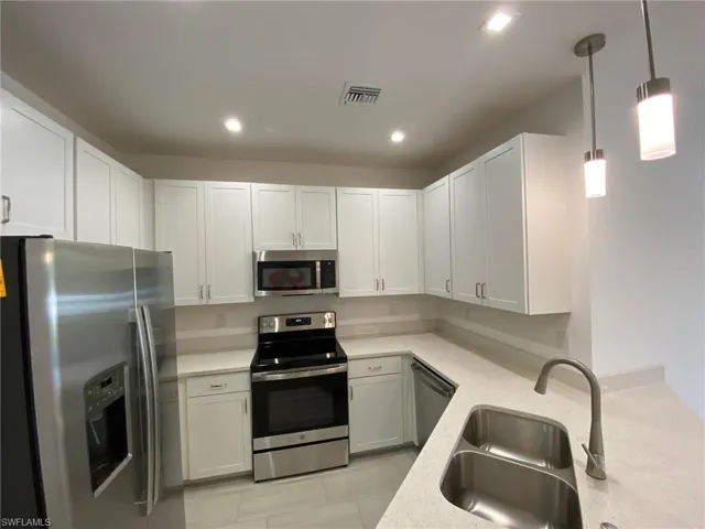Modern kitchen featuring white shaker cabinetry, stainless steel appliances, light-toned countertops, a double basin sink, and recessed lighting with pendant fixtures