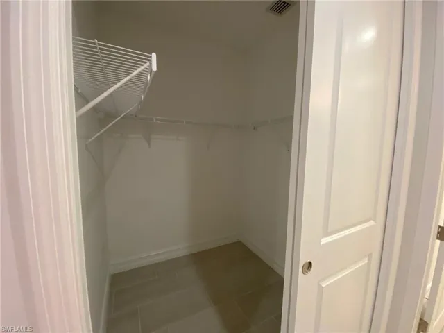 Recessed walk-in closet featuring light-toned tile flooring, white wire shelving, and a white interior door with a silver-tone handle