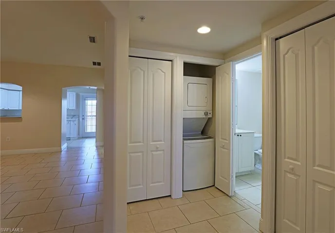 Laundry area with arched walkways, light tile patterned floors, stacked washing machine and dryer, and recessed lighting