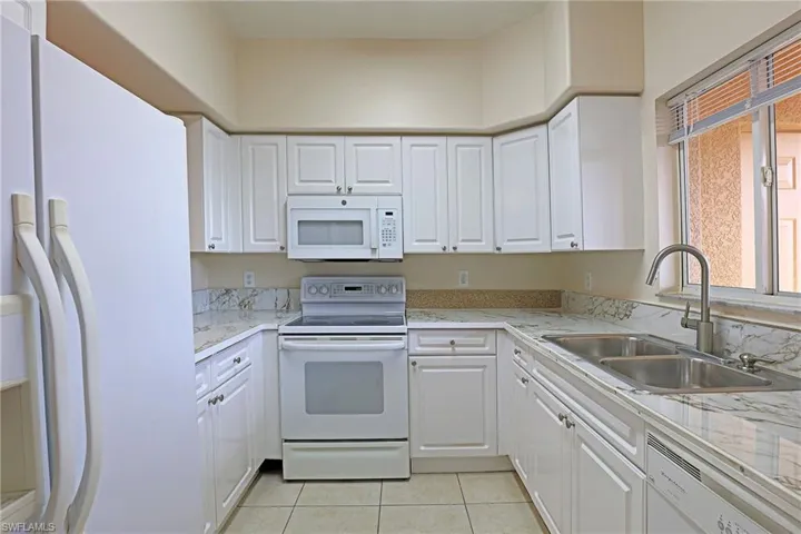 Kitchen featuring white appliances, white cabinets, light tile patterned floors, and light stone counters