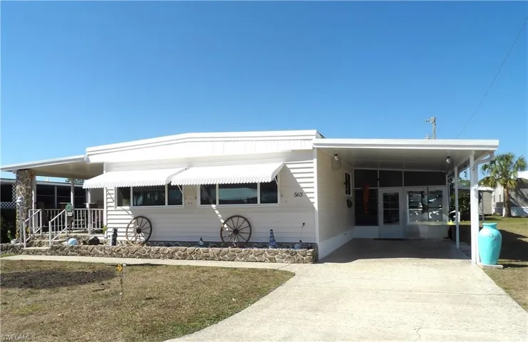 Manufactured / mobile home featuring concrete driveway, a carport, a front yard, and covered porch