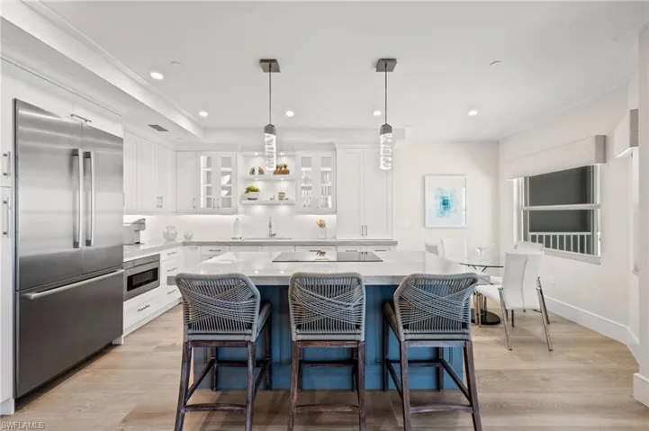 Kitchen with a kitchen island, built in appliances, pendant lighting, white cabinets, and light wood-type flooring