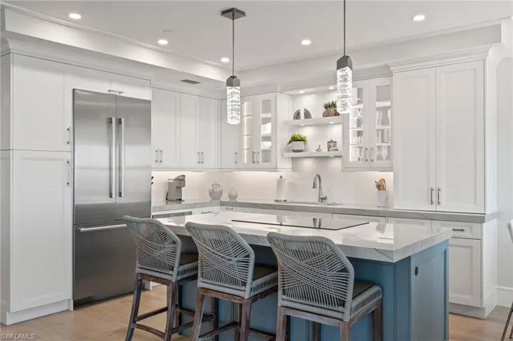 Kitchen with white cabinets, a center island, stainless steel built in fridge, and a breakfast bar area