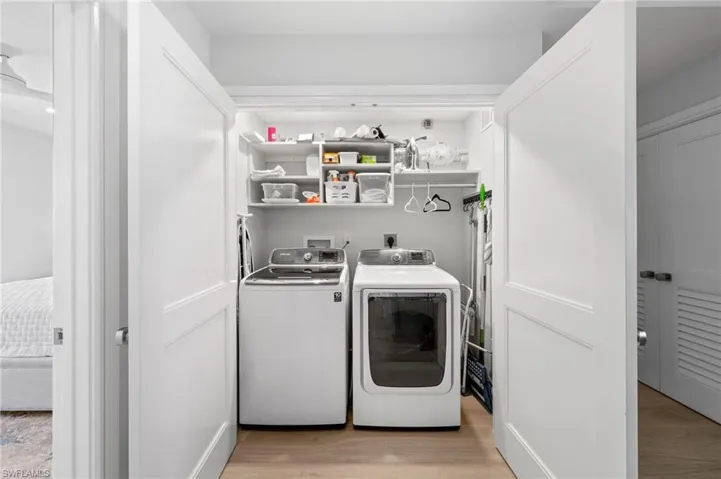 Clothes washing area with washing machine and clothes dryer and light hardwood / wood-style flooring
