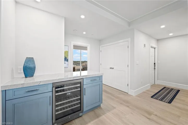 Kitchen featuring light stone countertops, light hardwood / wood-style floors, kitchen peninsula, and beverage cooler