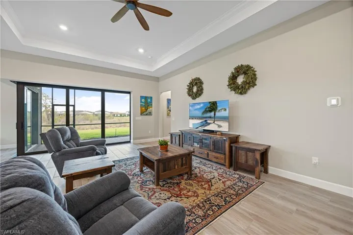 Living room featuring light wood finished floors, crown molding, a tray ceiling, recessed lighting, and a ceiling fan