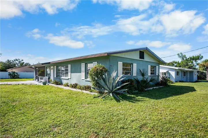 Single-story residence featuring light blue stucco siding, white window shutters, a low-slope roofline, and established landscaping