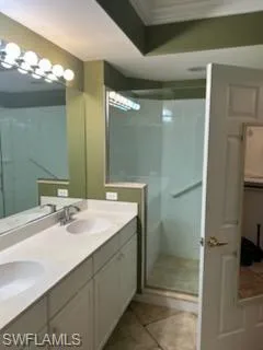 Dual vanity with integrated sinks and white cabinetry, complemented by a glass-enclosed shower, decorative wall molding, and tiled flooring