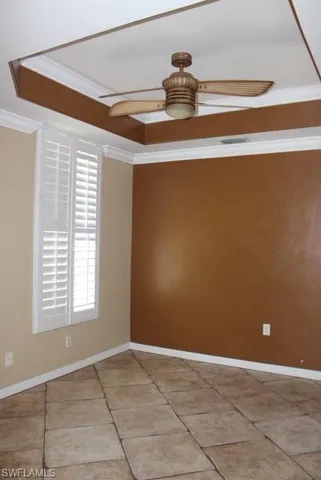Room featuring a tray ceiling with a ceiling fan, crown molding, plantation shutters, and large format floor tiles