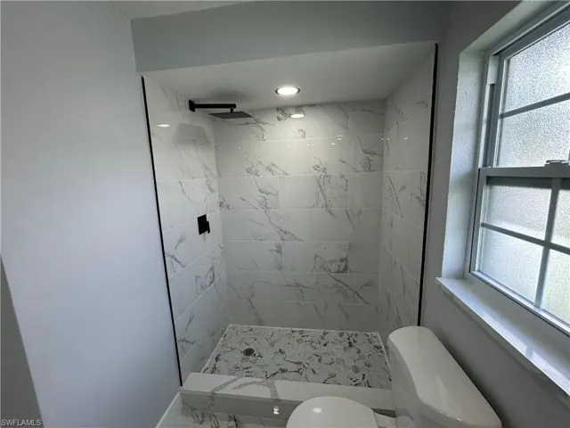 Bathroom featuring plenty of natural light, a tile shower, and toilet