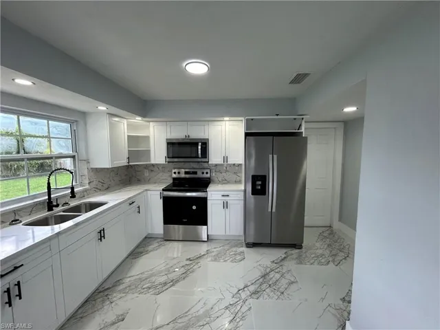 Kitchen with light tile patterned flooring, appliances with stainless steel finishes, sink, and decorative backsplash