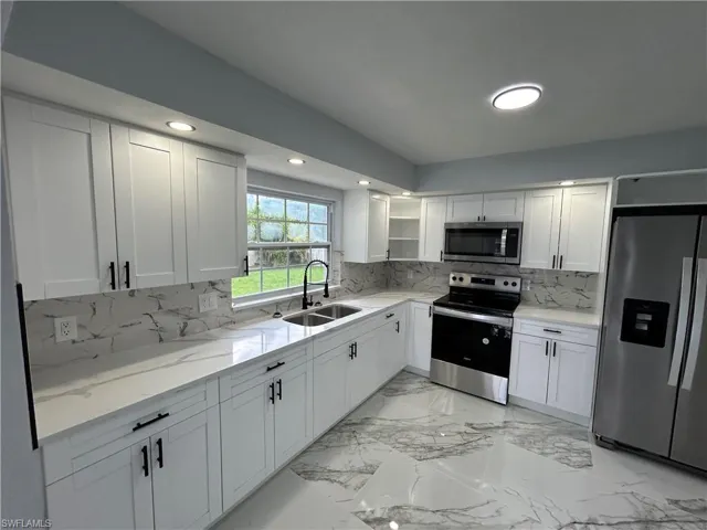 Kitchen featuring backsplash, stainless steel appliances, white cabinetry, sink, and light stone countertops