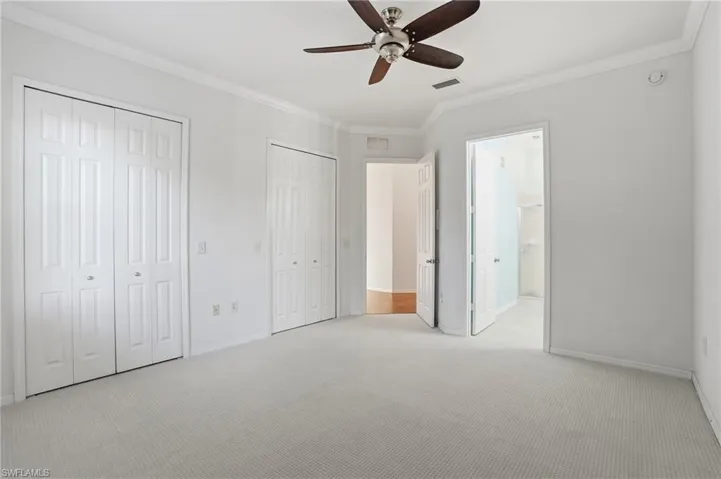 Unfurnished bedroom with two closets, crown molding, carpet, ceiling fan, and connected bathroom