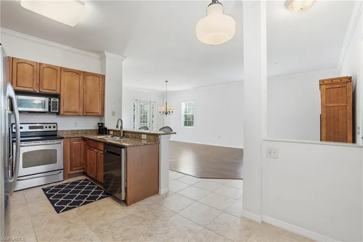 Kitchen featuring appliances with stainless steel finishes, pendant lighting, crown molding, brown cabinetry, and a peninsula