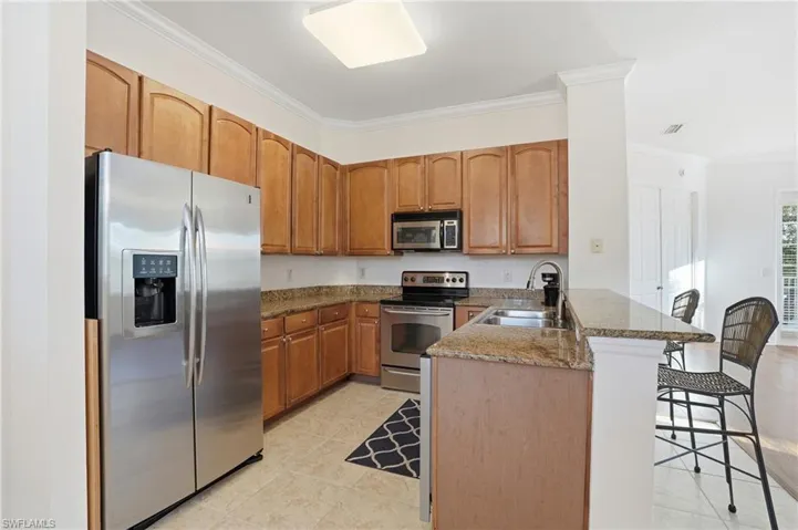 Kitchen featuring stainless steel appliances, a peninsula, ornamental molding, dark stone countertops, and a breakfast bar area