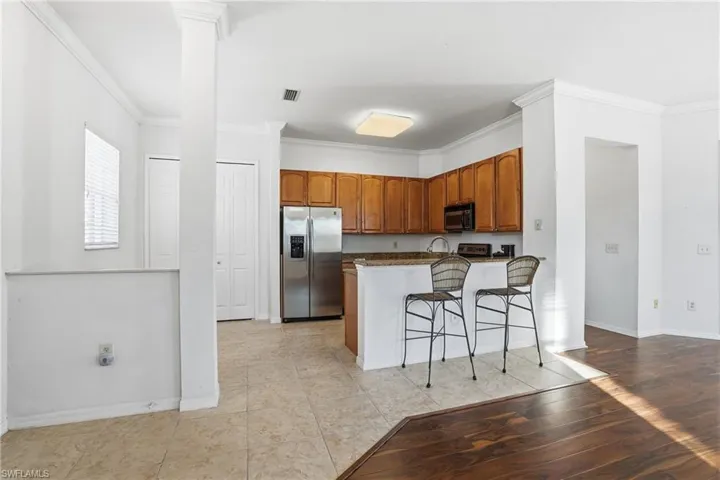 Kitchen with crown molding, a breakfast bar, appliances with stainless steel finishes, brown cabinetry, and dark stone counters
