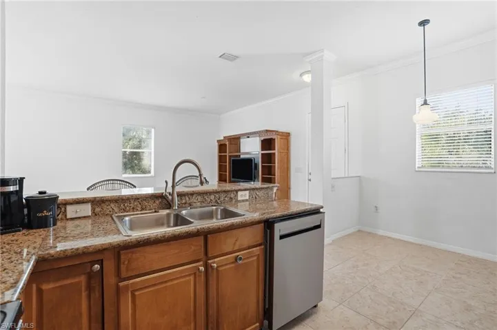 Kitchen featuring brown cabinetry, dishwasher, crown molding, pendant lighting, and light tile patterned floors