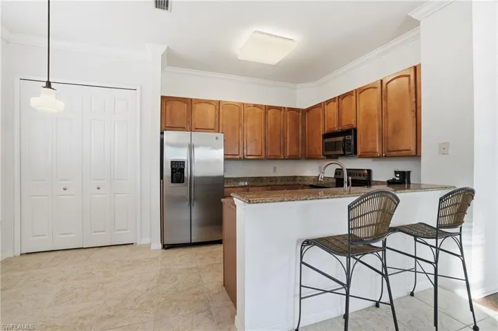 Kitchen featuring brown cabinetry, dark stone counters, black appliances, ornamental molding, and a peninsula