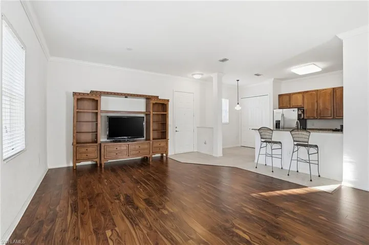 Unfurnished living room with crown molding, dark wood-type flooring, and decorative columns
