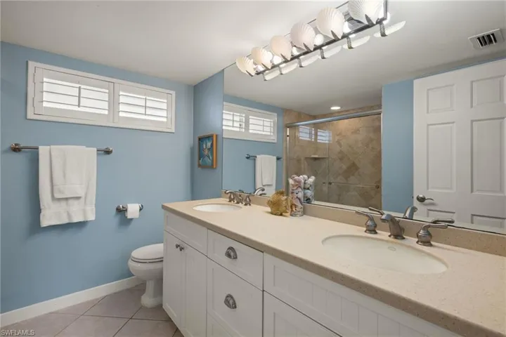 Full bath with light tile patterned floors, double vanity, and a shower stall