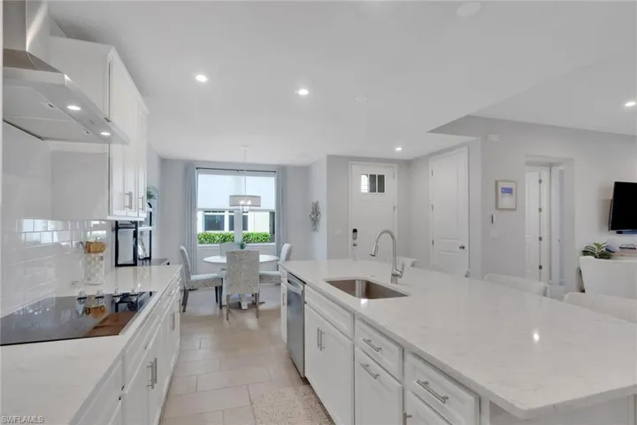 Kitchen with white cabinets, a kitchen island with sink, light stone countertops, black electric cooktop, and recessed lighting