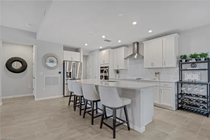 Kitchen featuring a breakfast bar area, white cabinetry, stainless steel appliances, an island with sink, and light stone countertops