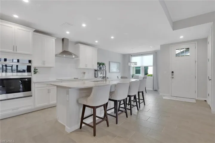 Kitchen with a center island with sink, a breakfast bar, white cabinetry, double oven, and pendant lighting