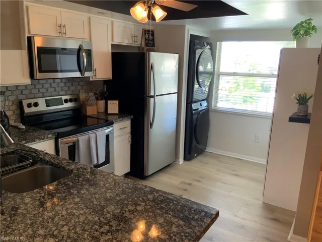 Kitchen with stacked washer / drying machine, stainless steel appliances, decorative backsplash, and white cabinetry